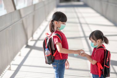 Coronavirus salgını sırasında okula giderken maske takan küçük bir kız ve kız kardeş. Hastalığı önlemek için güvenlik maskesi. Anne ve çocuk covid 19 salgınında okuldalar.. 