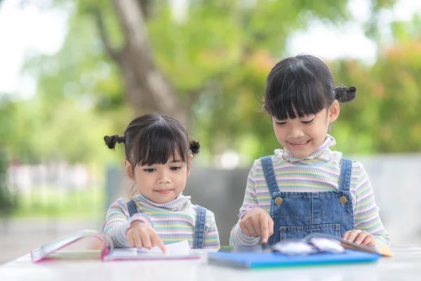 Two student little Asian girls reading the book on table