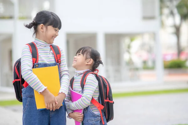 回学校去两个可爱的亚洲女孩 背着书包 在学校里一起举着一本书 — 图库照片