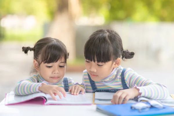 Two student little Asian girls reading the book on table