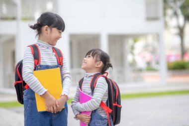 Okula dönelim. Okul çantalı iki tatlı Asyalı kız çocuğu okulda kitap tutuyorlar.