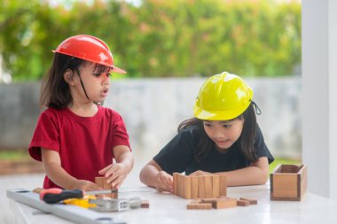Mühendislik şapkası takan Asyalı kardeşler tahta oyuncaktan ev yapıyorlar. Öğrenmeye ve geliştirmeye, küçük mimar..