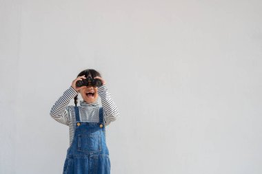 Beyaz arka planda dürbünle bakan küçük Asyalı kız. Keşif ve macera konsepti.