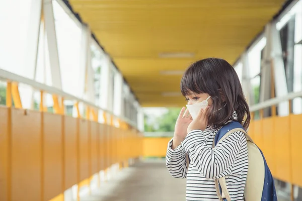 School child wearing a face mask during coronavirus and flu outbreak. Little girl going back to school after covid-19 quarantine and lockdown.