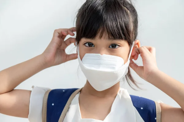 白い背景のアジア系の少女は コロナウイルス病の蔓延を防ぐフェイスマスクを着用しています 彼女の顔に外科マスクを持つ女の子のクローズアップ — ストック写真