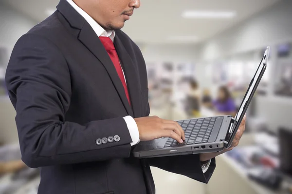 Liikemies työskentelee kannettavan tietokoneen toimiston taustalla — kuvapankkivalokuva