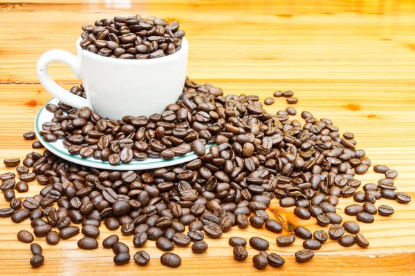 Kaffebönor på cup och träbord — Stockfoto