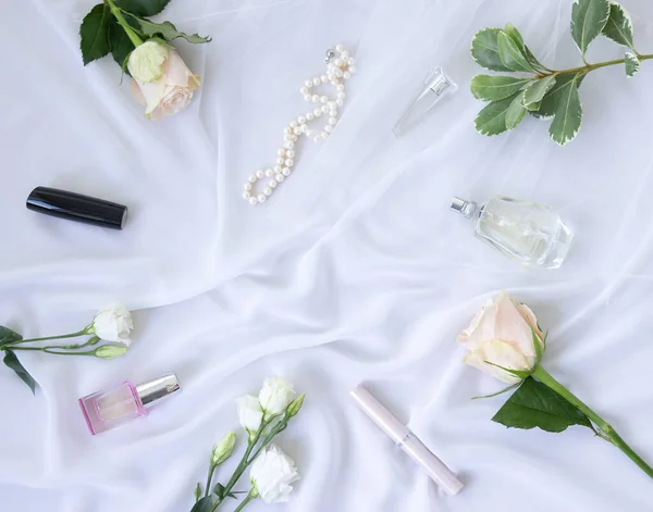 Perfume, flowers, jewelry, pearl, cosmetics on a white chiffon background. Feminine elegant fashion concept. Flat lay.