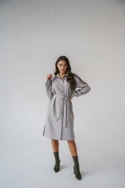 Gri stüdyo arka planında poz veren gündelik sonbahar kıyafetleri giyen genç bir esmerin portresi.