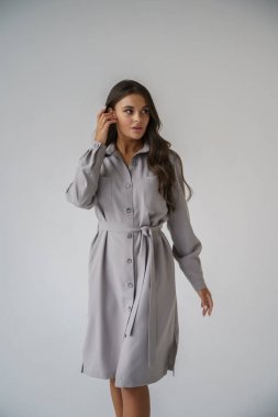 Gri stüdyo arka planında poz veren gündelik sonbahar kıyafetleri giyen genç bir esmerin portresi.