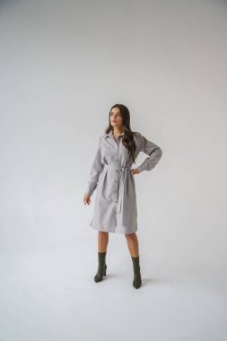 Gri stüdyo arka planında poz veren gündelik sonbahar kıyafetleri giyen genç bir esmerin portresi.