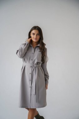 Gri stüdyo arka planında poz veren gündelik sonbahar kıyafetleri giyen genç bir esmerin portresi.