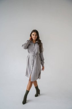 Gri stüdyo arka planında poz veren gündelik sonbahar kıyafetleri giyen genç bir esmerin portresi.