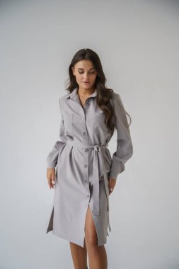 Gri stüdyo arka planında poz veren gündelik sonbahar kıyafetleri giyen genç bir esmerin portresi.