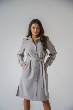 Gri stüdyo arka planında poz veren gündelik sonbahar kıyafetleri giyen genç bir esmerin portresi.