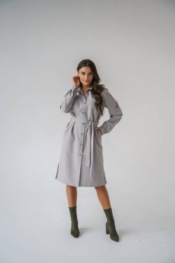 Gri stüdyo arka planında poz veren gündelik sonbahar kıyafetleri giyen genç bir esmerin portresi.