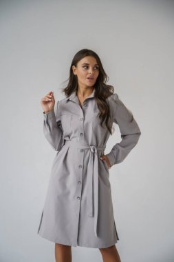 Gri stüdyo arka planında poz veren gündelik sonbahar kıyafetleri giyen genç bir esmerin portresi.