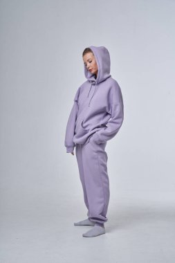 Beyaz stüdyo arka planında duran mor spor elbiseli sarışın güzel kadının stüdyo portresi. 