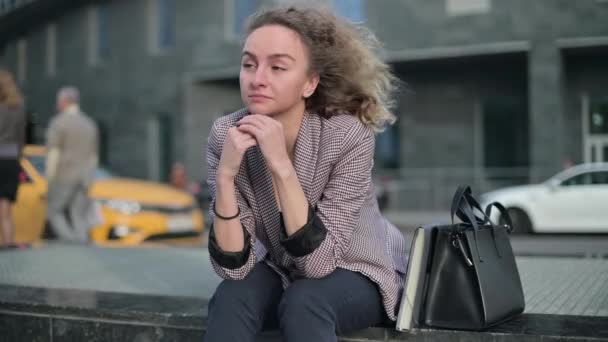 Mladá zamyšlená žena o něčem přemýšlí, zatímco sedí na ulici — Stock video