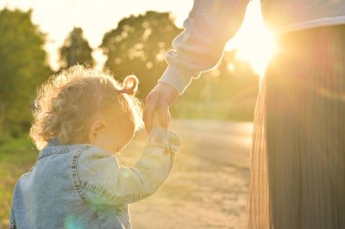 Anne, akşam gün batımında yürürken küçük kızının elini tutuyor. Kameranın objektifinde güneş ışınları parlıyor