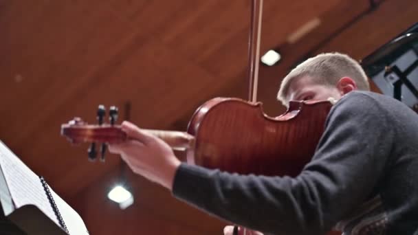 Onderaanzicht van een jonge man die viool speelt met een strijkorkest — Stockvideo