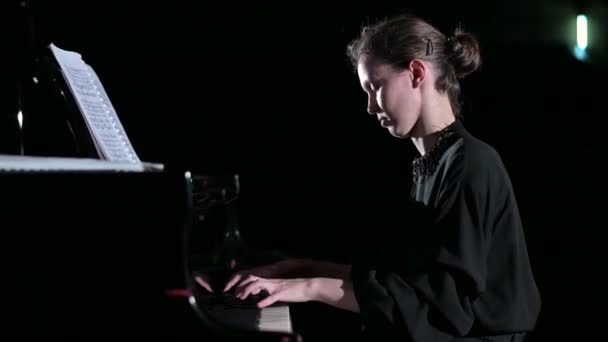 Una joven toca tranquilamente el piano en el centro de atención del escenario — Vídeo de stock