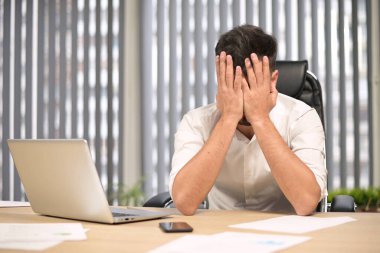 Genç bir lider ofisteki işyerinde oturur ve bir noktada yorgun bir şekilde bakar, yüzünü ellerine saklar. Müdür çalışmaktan yoruldu.