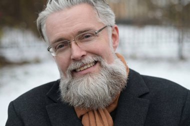 Kış sabahı parkta gülümseyen gri saçlı adamın portresi.