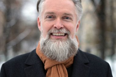 Dost canlısı gri saçlı adamın portresi. Bir kış günü kameraya bakar ve açık havada gülümser.