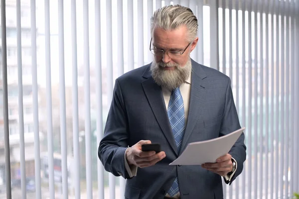 The mature gray-haired company executive examines the reports. The boss is not happy with the performance and is upset. Portrait of an adult gray-haired man in the office