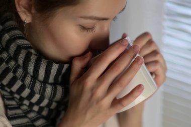 Sıcak bir içecek soğuk semptomları olan bir kadını ısıtır ve iyileştirir. Kışın sıcak bir içecekle tedavi edilen bir kadının yakın çekimi.