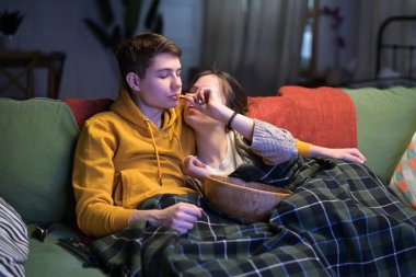 Genç bir adam ve kız arkadaşı akşamları kanepede televizyon izleyip cips yiyorlar. Genç çift birlikte harika vakit geçiriyor.