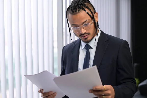 Un joven y elegante empleado de oficina negro inusual examina los documentos recibidos — Foto de Stock