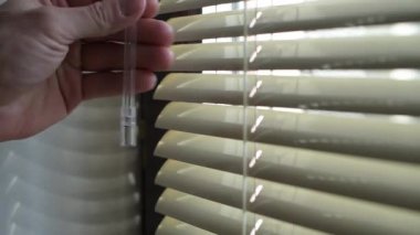 Kapı kolunu çevirerek perdeleri açar, sokaktan içeri ışık girer.