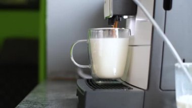 Kahve makinesi, cam bardağa sütlü espresso döker..