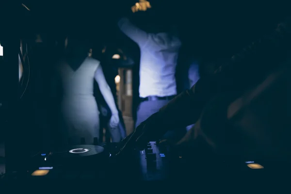 Dj mixes the track in nightclub at party with dancing people on blur background — Stock Photo, Image