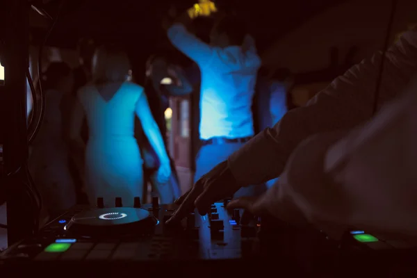 Dj mezcla la pista en el club nocturno en la fiesta con gente bailando en un fondo borroso Imagen de stock