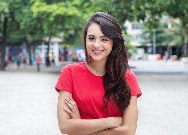 Çapraz kolları açık bir parkta olan kırmızı gömlekli genç kadın