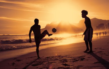 Gün batımında Rio kumsalda futbol oynayan iki adam
