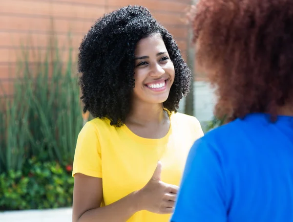 Laughing latin woman with curly black hair talking with girlfrie