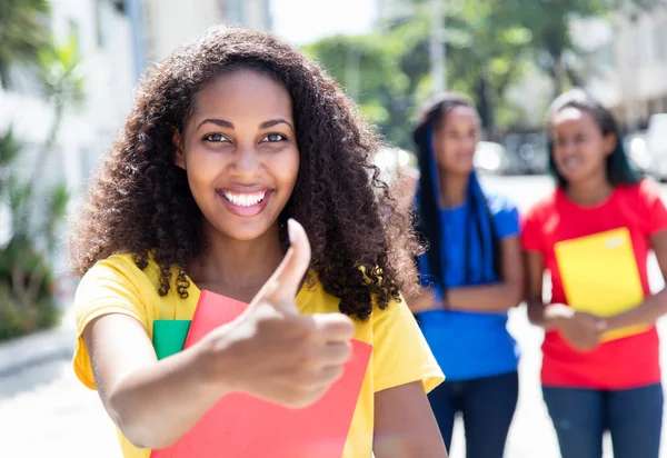 Estudiante caribeño mostrando pulgar en la ciudad con amigos —  Fotos de Stock