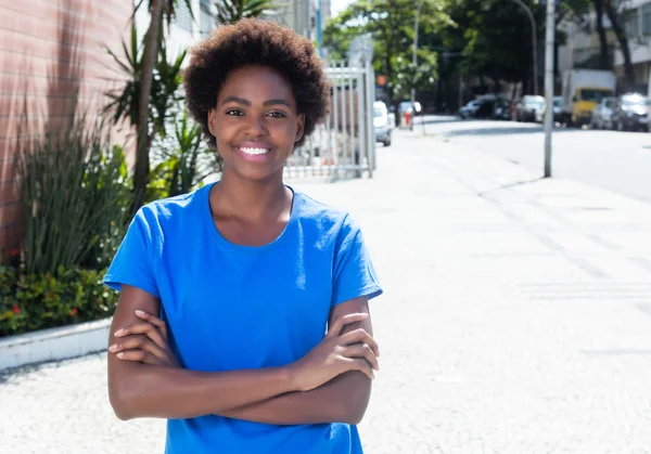 Mujer africana con brazos cruzados en una camisa azul al aire libre en la ciudad —  Fotos de Stock