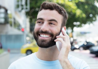Sakallı beyaz adam telefon açık şehirde gülüyor