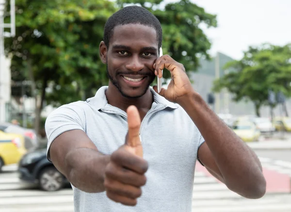 Riendo hombre africano con barba en el teléfono mostrando el pulgar hacia arriba — Foto de Stock