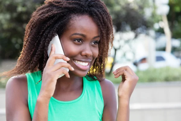 Afrikansk kvinna i en grön skjorta utomhus på telefon — Stockfoto