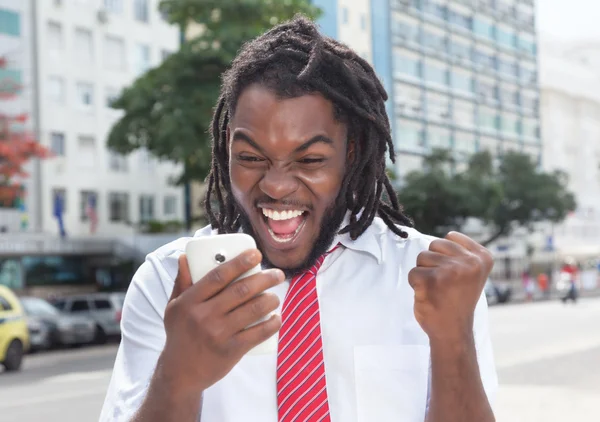 Cheering african american businessman with dreadlocks and phone — Stock Photo, Image