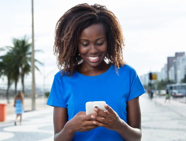 Skrattande afrikansk kvinna i en blå skjorta skicka meddelande med phon — Stockfoto