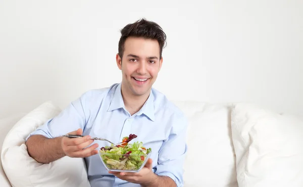 Tipo hispano sentado en un sofá y comiendo ensalada — Foto de Stock