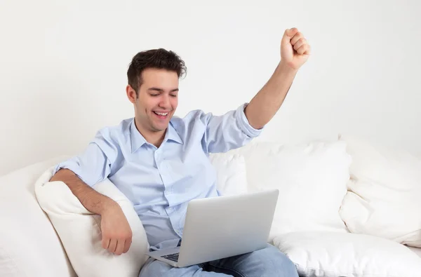 Juichende Spaanse man met laptop op een sofa — Stockfoto