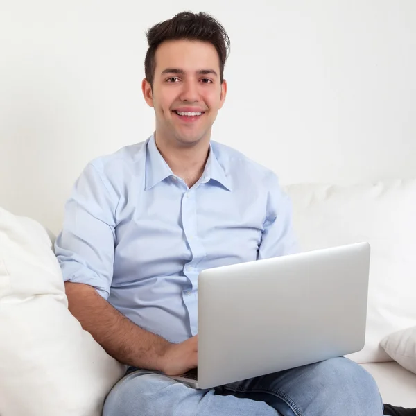 Spaanse man met laptop lachen op een sofa — Stockfoto